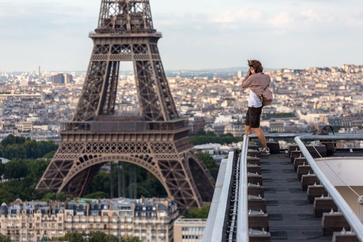 chico sobre un edificio sacando una fotografía de la torre Eifel 