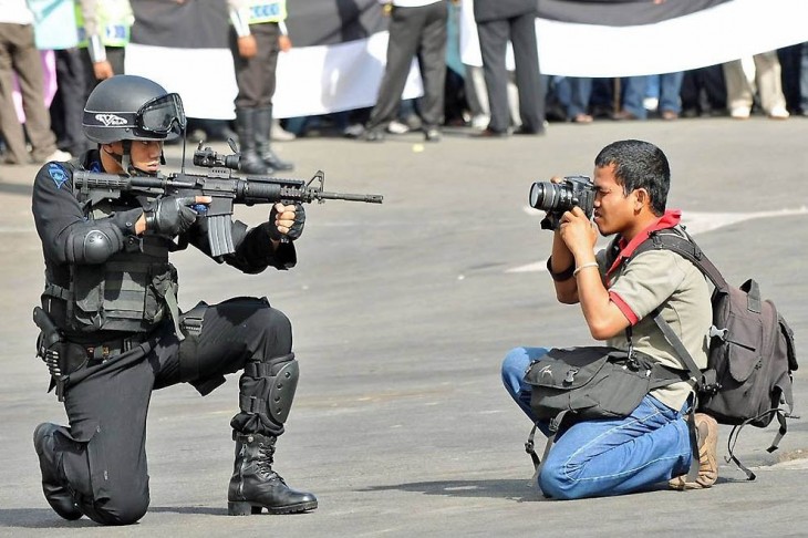 chico tomando una fotografía frente aun hombre señalándolo con un arma 