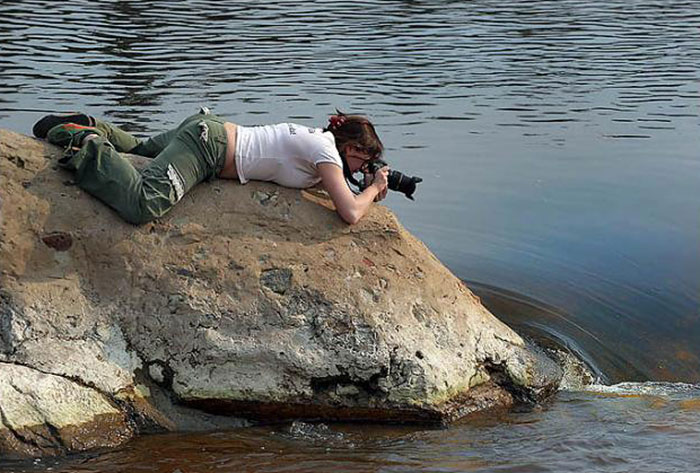 Una mujer tomando una foto acostada en una roca 