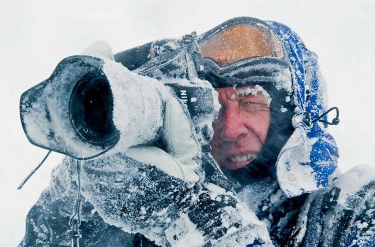 hombre tomando una fotografía con hielo alrededor de él y de su cámara 