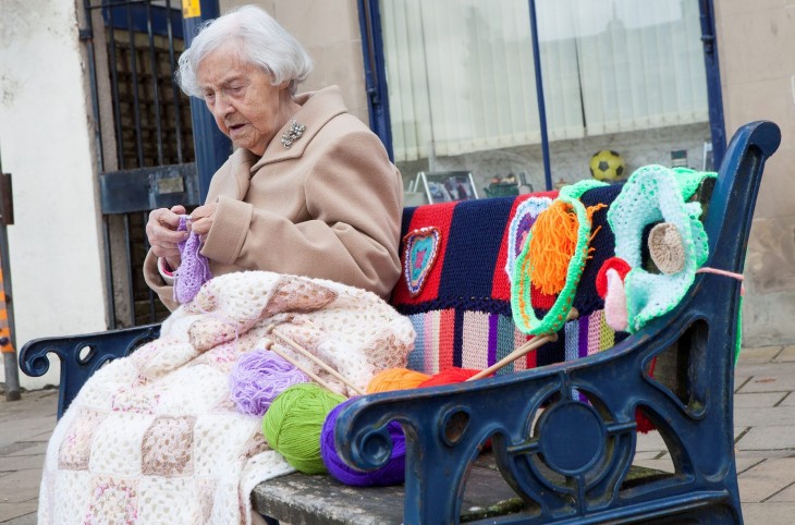 Mujer sentada en la banca de un parque en Escocia tejiendo 