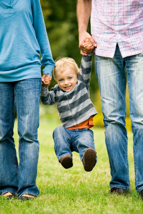 Dos personas balanceando a un niño directamente de las manos 