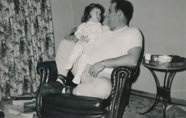 Fotografía de un hombre sentado en un sillón con una niña en sus brazos 