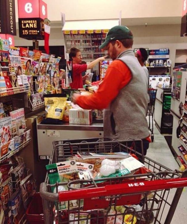 Un hombre con un carro de supermercado lleno de muchas cosas en la fila de una caja rápida 