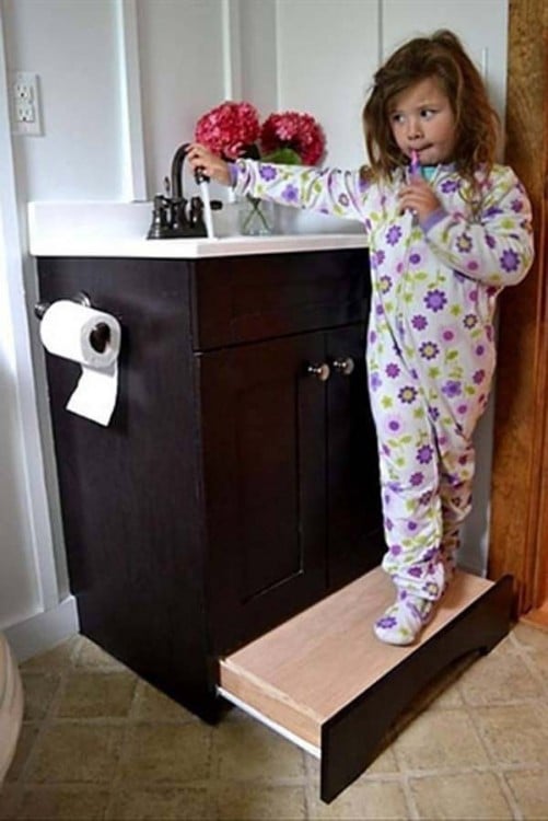 Niña sobre un escalón corredizo en el gabinete de baño 