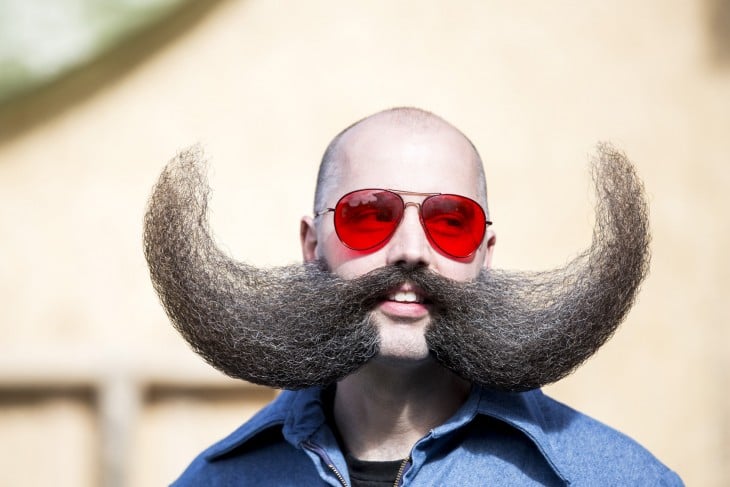 Cara de un hombre con lentes rojos y un bigote de gran tamaño 