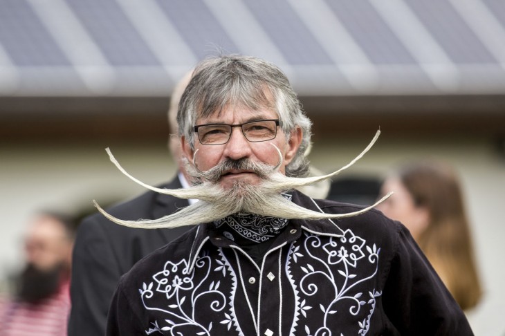 hombre de negro con una barba y bigote demasiado largo acomodado a los costados 