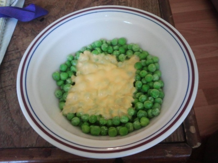 Platillo lleno de chicharos verdes con una rebanadita de queso 