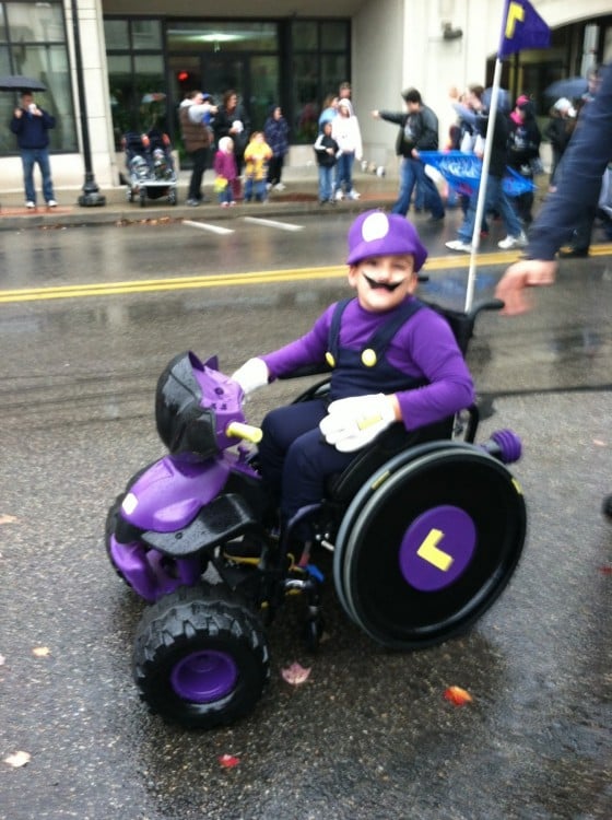 Niño con un disfraz de Waluigi de Mario Kart en su silla de ruedas 