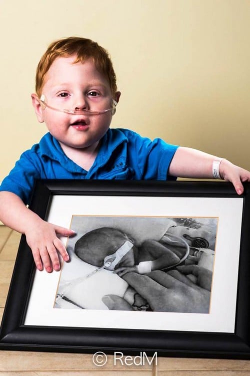 Niño pelirojo sentado en el suelo agarrando con sus manos un retrato de él cuando era un bebé 