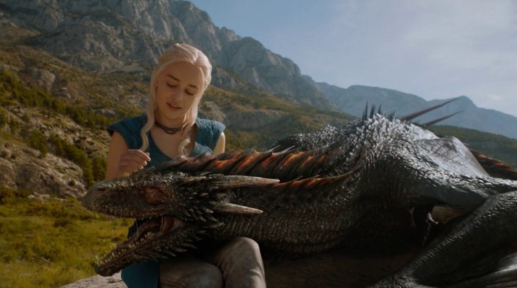 Daenerys Targaryen acariciando la cabeza de un dragón que esta sobre sus piernas 
