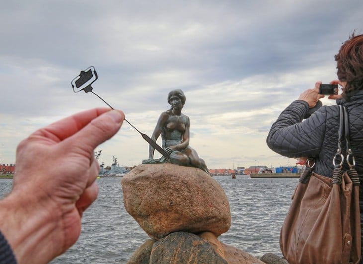 estatua de la sirenita en Copenhague, con un recorte de papel en su mano 