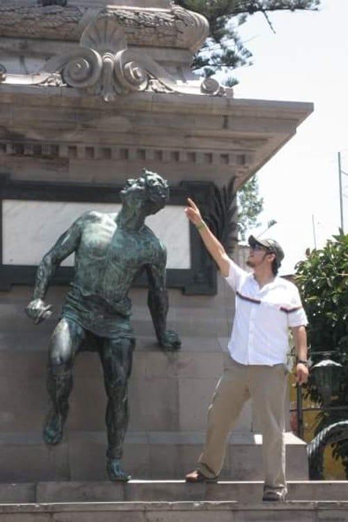 foto de un chico que esta señalando algo a un costado de una estatua que parece estar volteando 