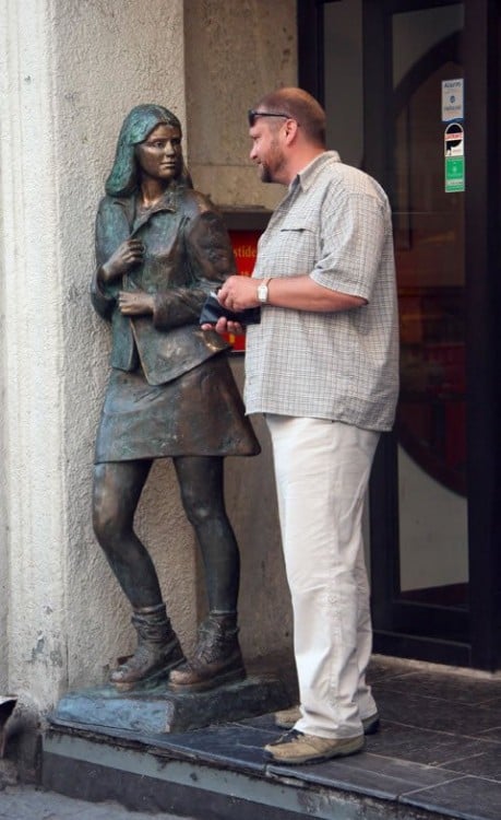 foto de un hombre con la cartera en la mano a un lado de una estatua con figura de chica en minifalda 