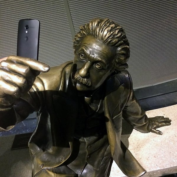 estatua de albert einstein con un celular simulando tomarse una selfie 
