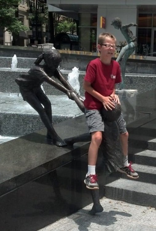 foto de un niño arriba de una estatua con cara de tristeza 