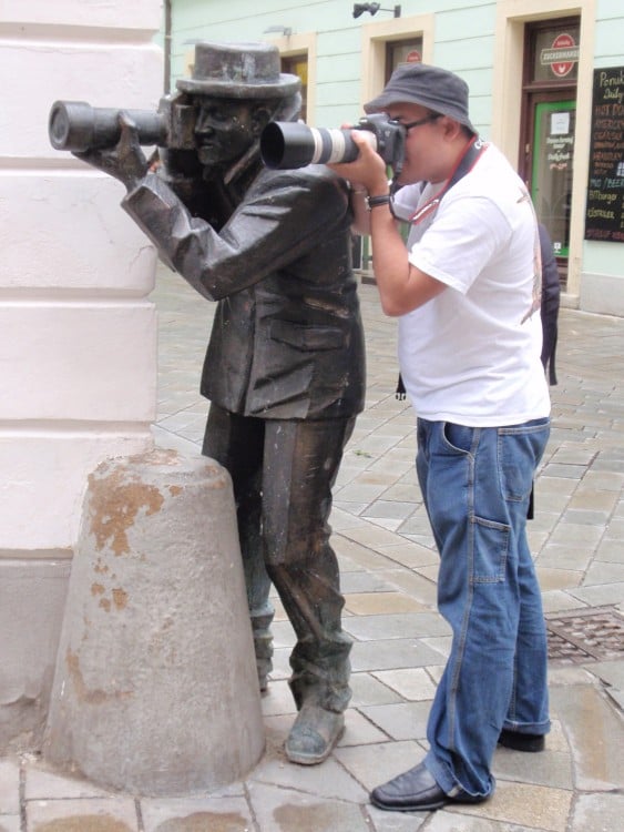 chico a un costado de una estatua que parece estar tomando una fotografía 