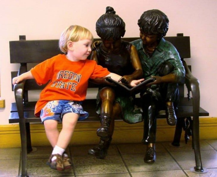foto de un niño con dos estatuas de niño señalando un libro 