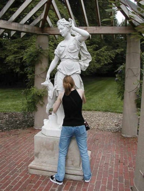 chica con la cara en medio de las piernas de una estatua 