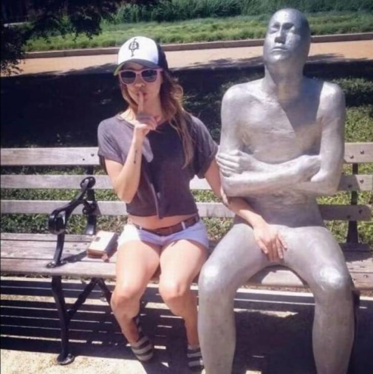 chica sentada a un costado de una estatua con su mano puesta entre las piernas de la estatua 