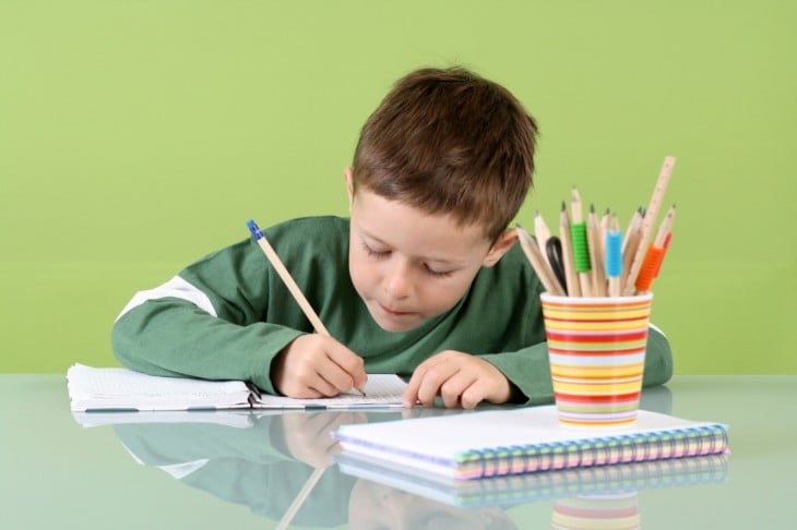 Niño escribiendo con lápiz sobre una hoja de papel 