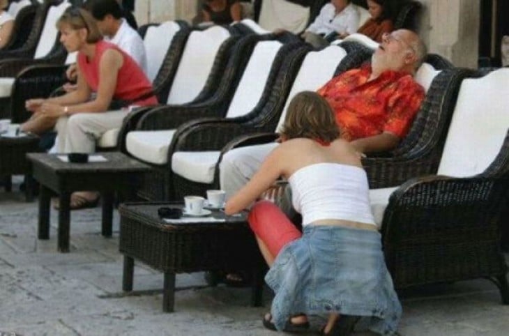 hombre sentado en un sillón dormido y a un lado una chica agachada 