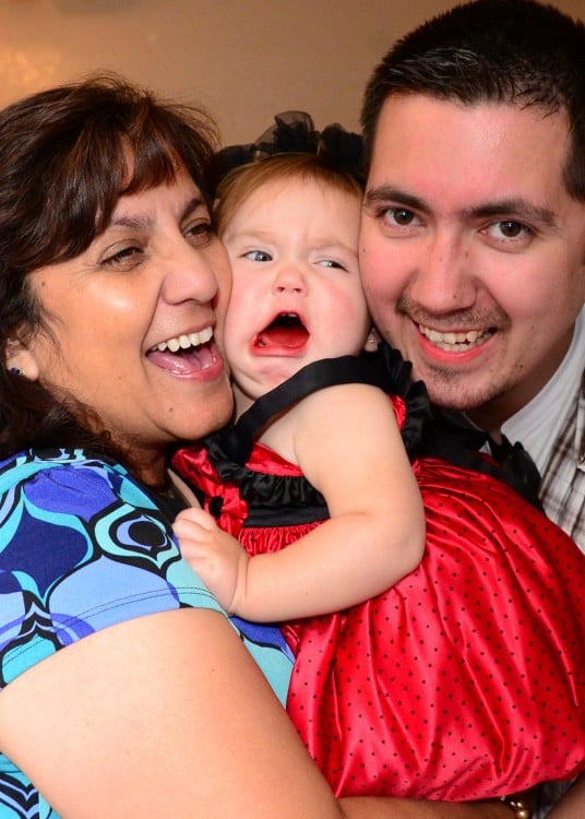 niña llorando mientras su abuela y su padre le aplastan la cara