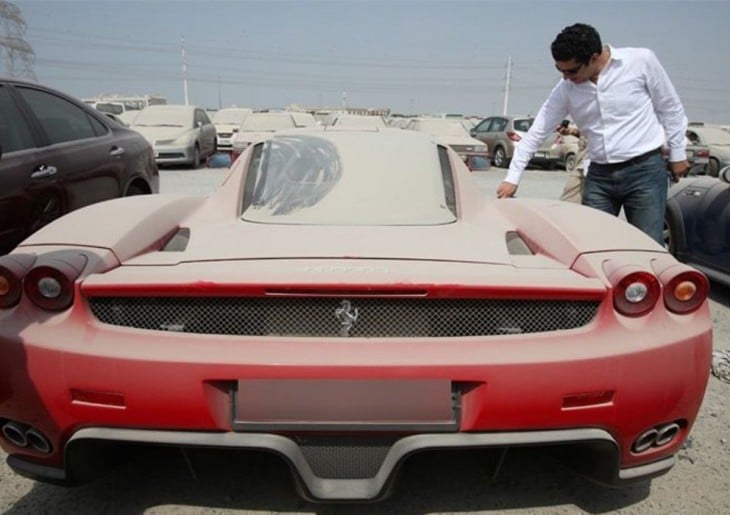 hombre dibujando sobre el polvo de un ferrari rojo abandonado en un estacionamiento de Dubai 