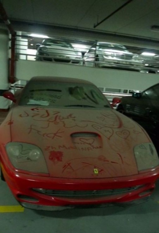 Ferrari rojo lleno de polvo dentro de un estacionamiento en Dubái 