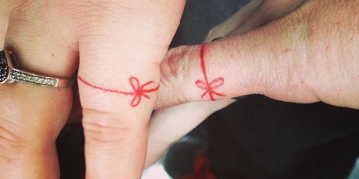 tatuaje de dos personas en el dedo meñique con un moño hecho en color rojo 