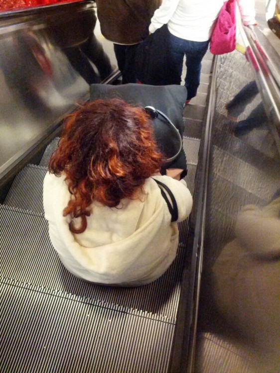 una mujer sentada en un escalón de las escaleras eléctricas 