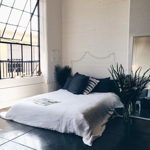 recámara con una cama cerca de una ventana con unas plantas a sus lados y pintada en color blanco 