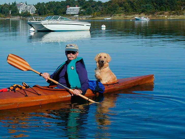 hombre dentro del kayak con un perro detrás 