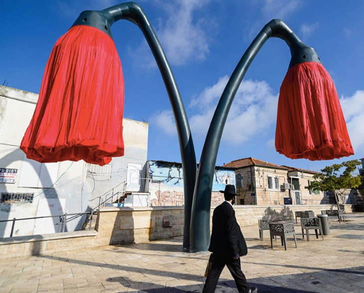 hombre caminando en la plaza Varsello de Jerusalén cerca de las lámparas de flores rojas 