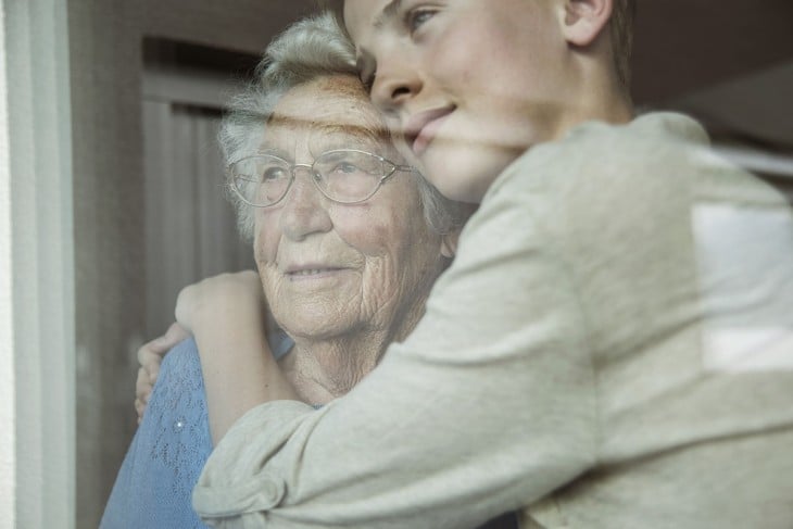 chica abrazando a su abuela a través de una ventana