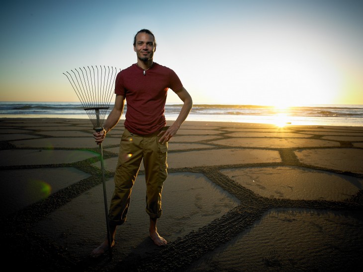 Andrés Amador con un rastrillo de jardín en una playa 