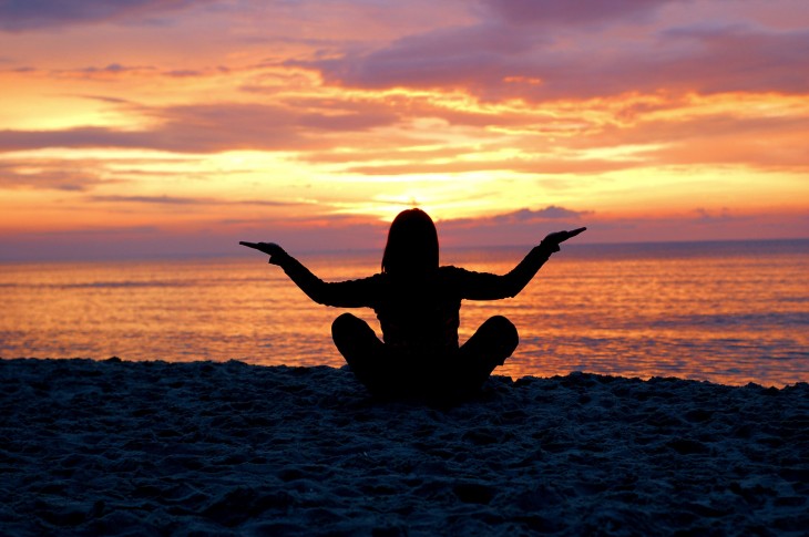 una mujer practicando yoga frente al mar al atardecer 