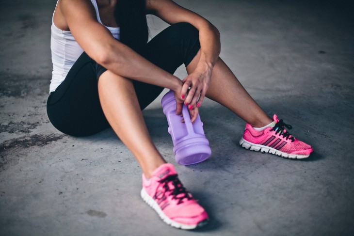 mujer con ropa deportiva sentada en el suelo con una botella de agua 