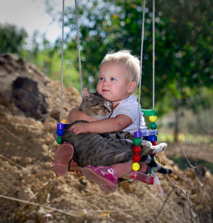 niño arriba de un columpio con su gato en las piernas 