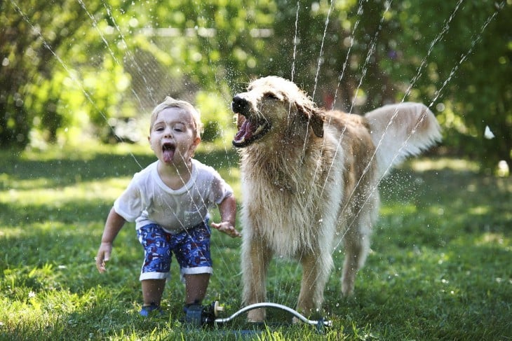 niño tomando agua en un jardín junto a su perro 