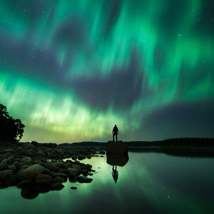 Hombre parado sobre una roca cerca de un lago en una noche en Finlandia 