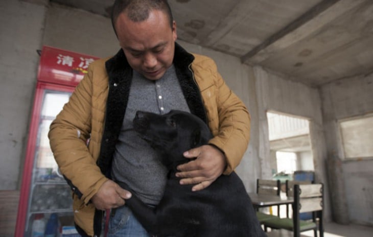 Hombre chino recargando a un perro sobre su cuerpo 