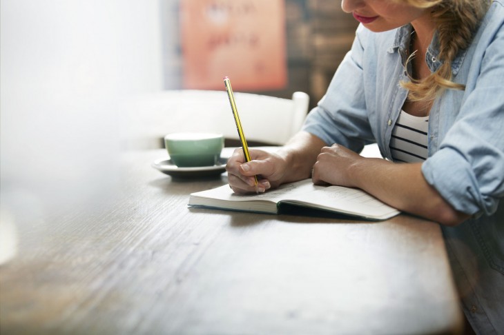 Chica sentada frente a un escritorio escribiendo en una libreta 