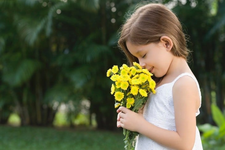 Niña oliendo un ramo de flores 