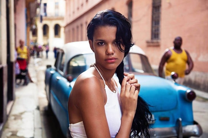 mujer cubana con un carro aziul al fondo
