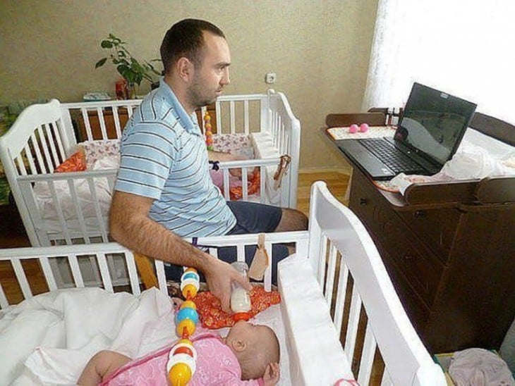 hombre dando de comer a sus dos bebés cada una en su cuna 