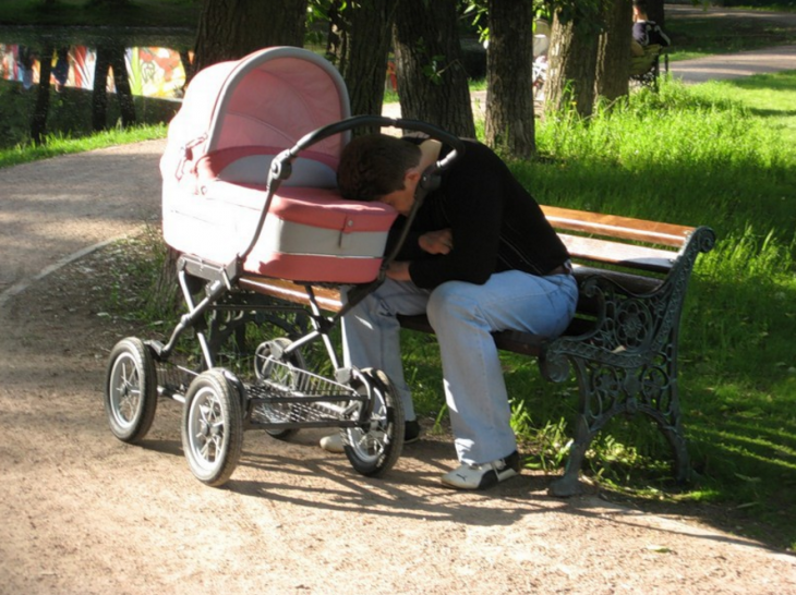 hombre dormido sobre la carriola de su bebé en un parque 