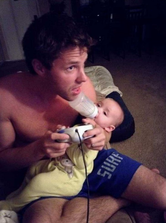 hombre jugando con su videojuego y dando biberón a su bebé 