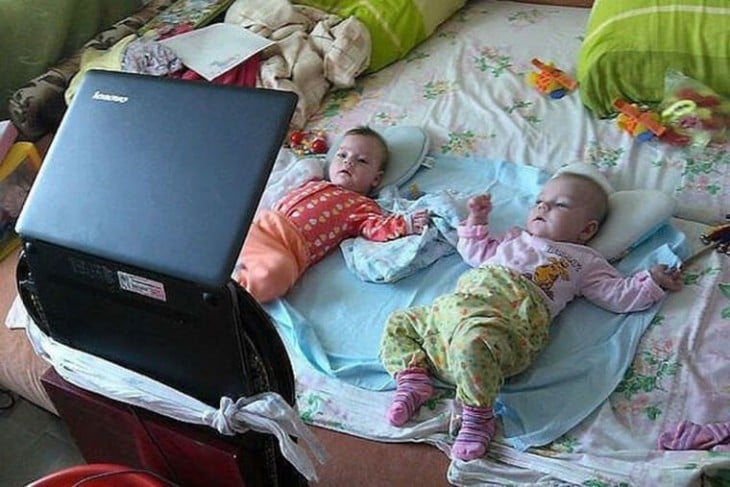 dos bebés acostadas en la cama viendo la computadora 