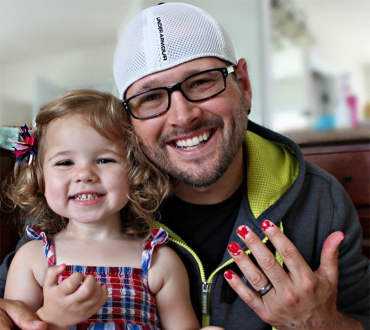 hombre sonriente mostrando sus uñas pintadas a lado de su hija 
